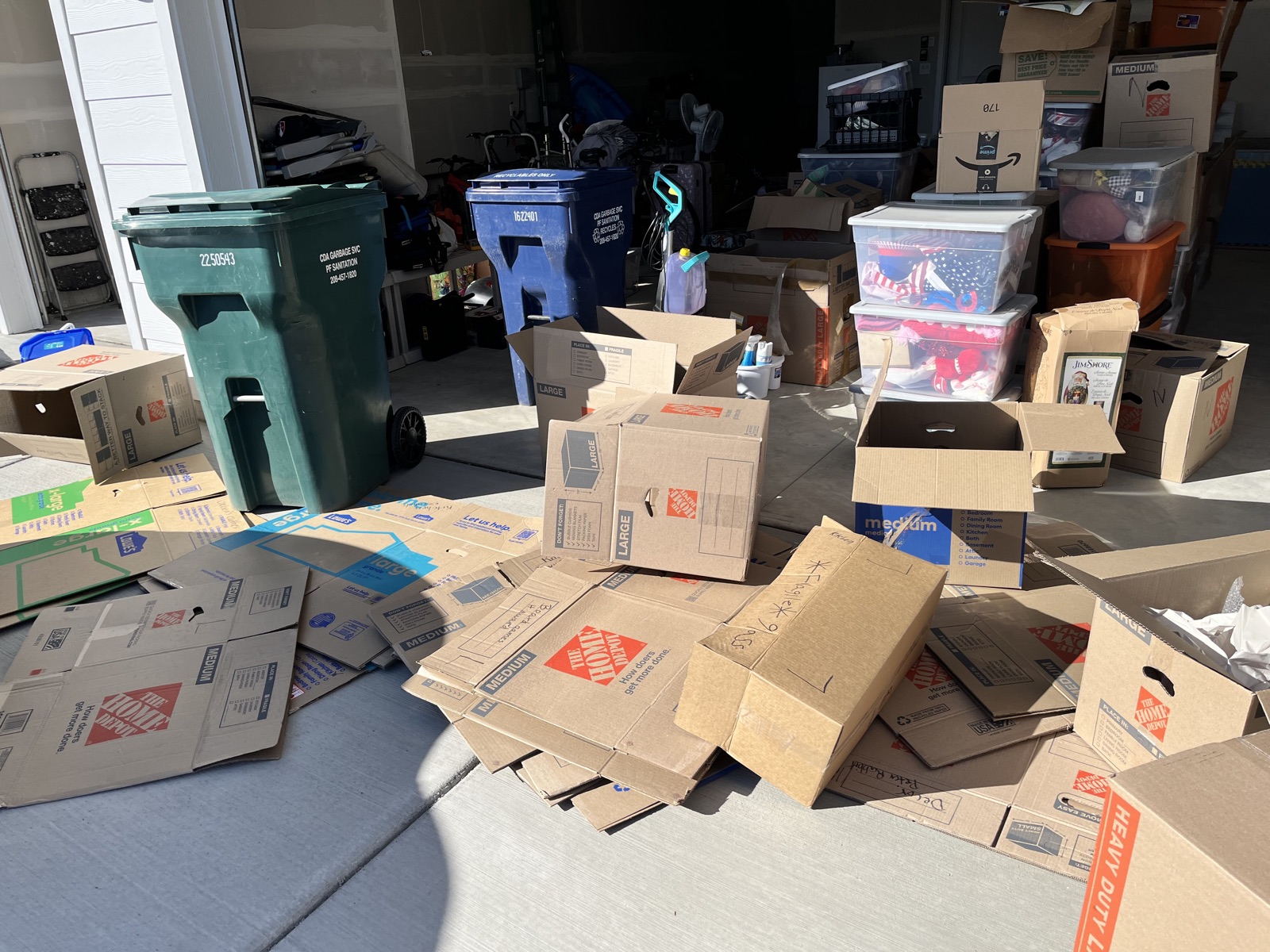 Garage floor and driveway covered in broken-down cardboard boxes and trash bins during a move